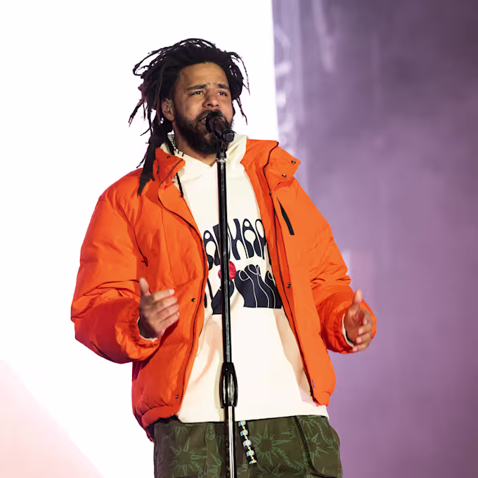 J. Cole performing onstage in an orange jacket on the Fall-Off Tour